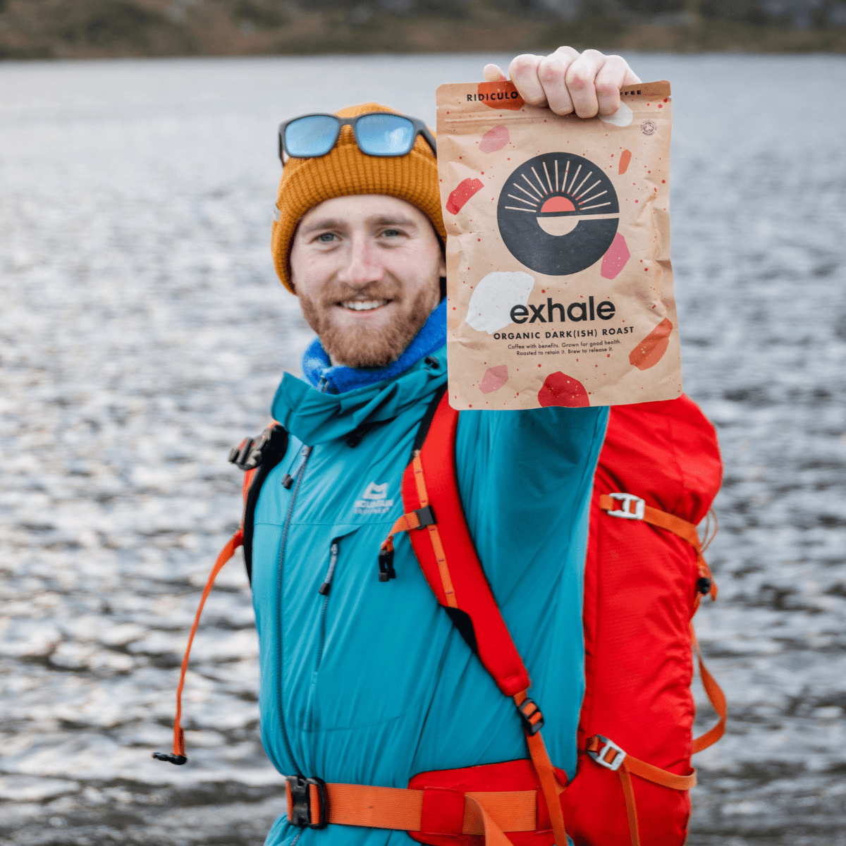 Person holding a bag of Organic Dark(ish) Roast Coffee by Exhale outdoors near water.
