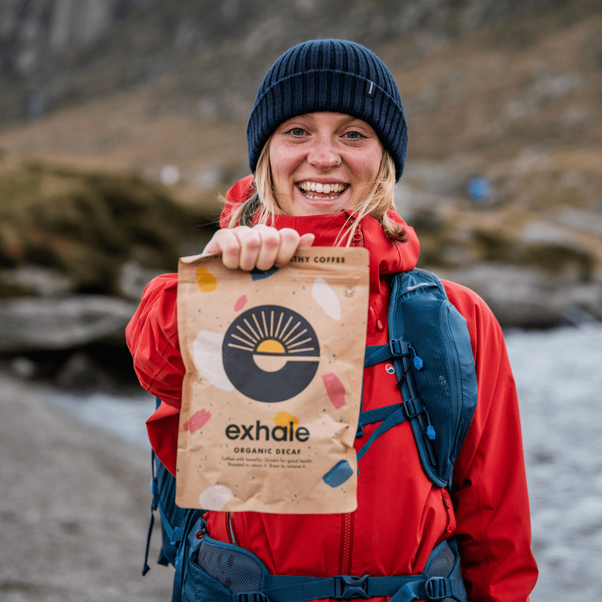 Woman holding Exhale Organic Decaf Coffee bag outdoors against a scenic backdrop.