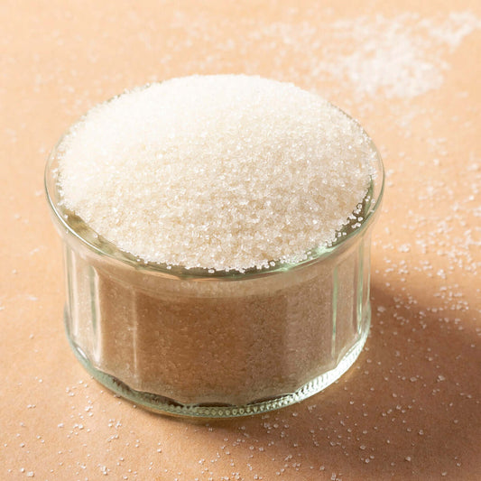 Glass container filled with white sugar on a beige background