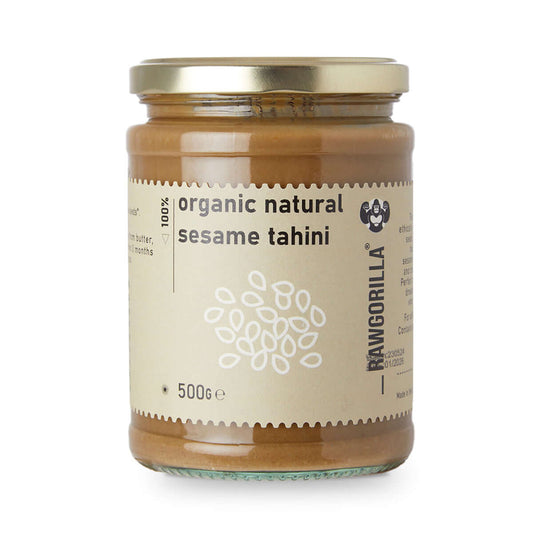 Jar of organic natural sesame tahini with a gold lid on a white background