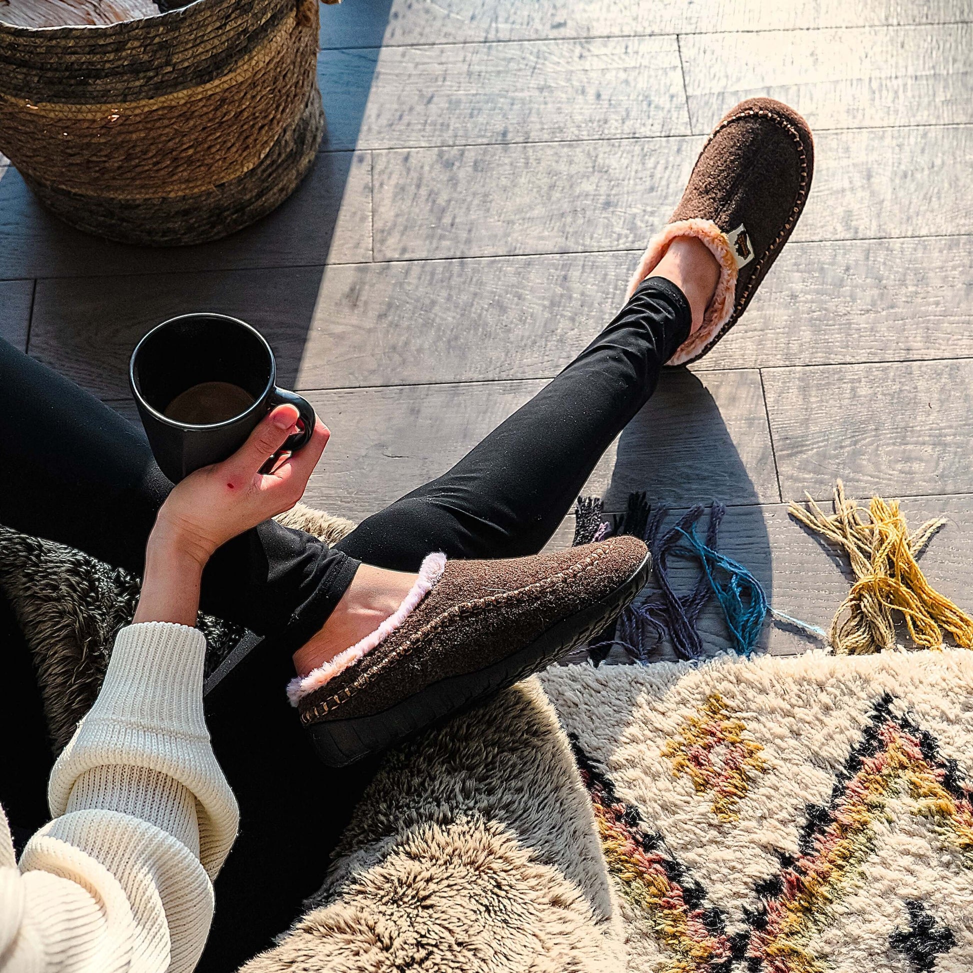 Woman wearing Ossa Low - Women's - Chocolate & Cream slippers, relaxing with a cup of coffee indoors.