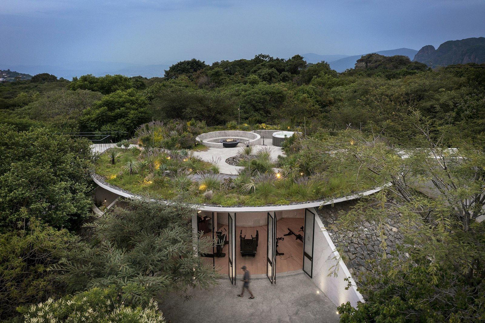 Round building with a green roof surrounded by trees and mountains