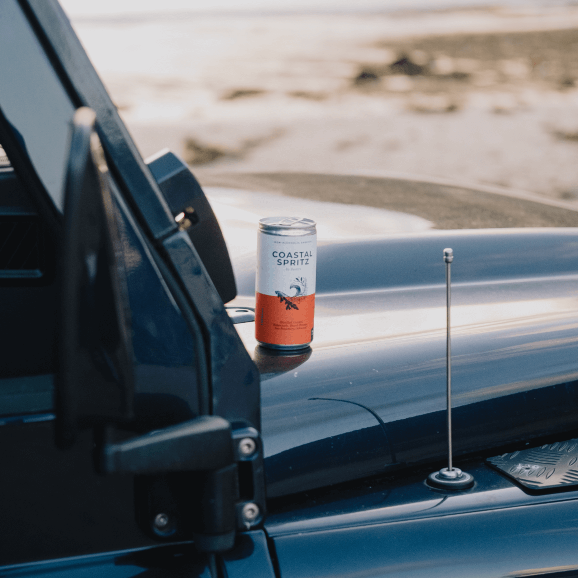 Pentire Coastal Spritz can placed on the hood of a vehicle against a coastal backdrop.
