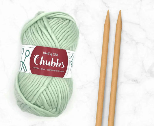 Peppermint Merino Super Chunky Weight yarn in mint green next to wooden knitting needles on a marble background.