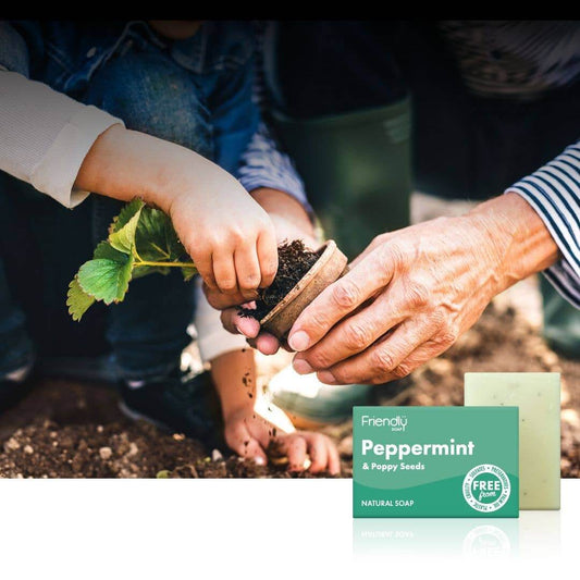 Two people planting a seed with a 'Friendly Soap' peppermint and poppy seeds bar soap in the foreground.