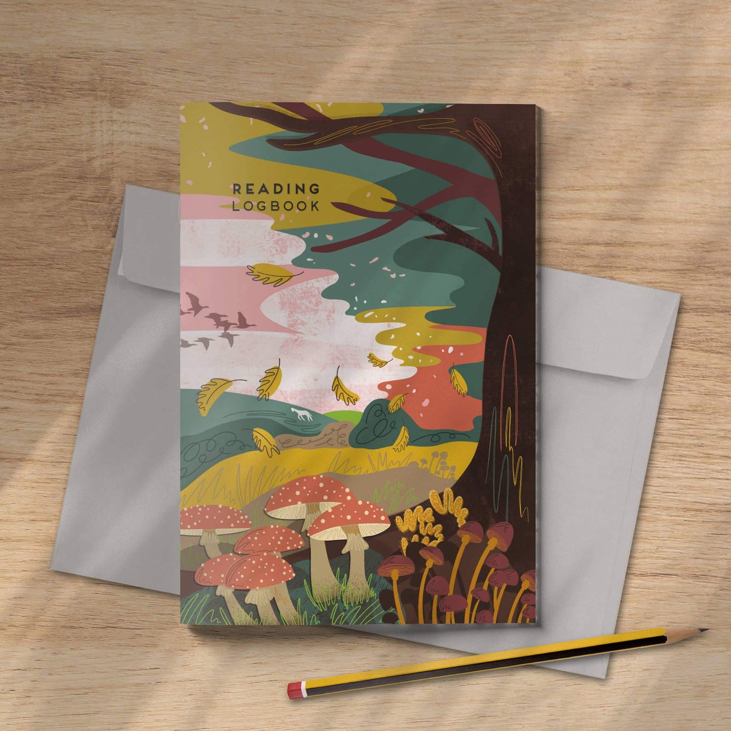 Decorative notebook with a forest design on a wooden surface with an envelope and pencil.