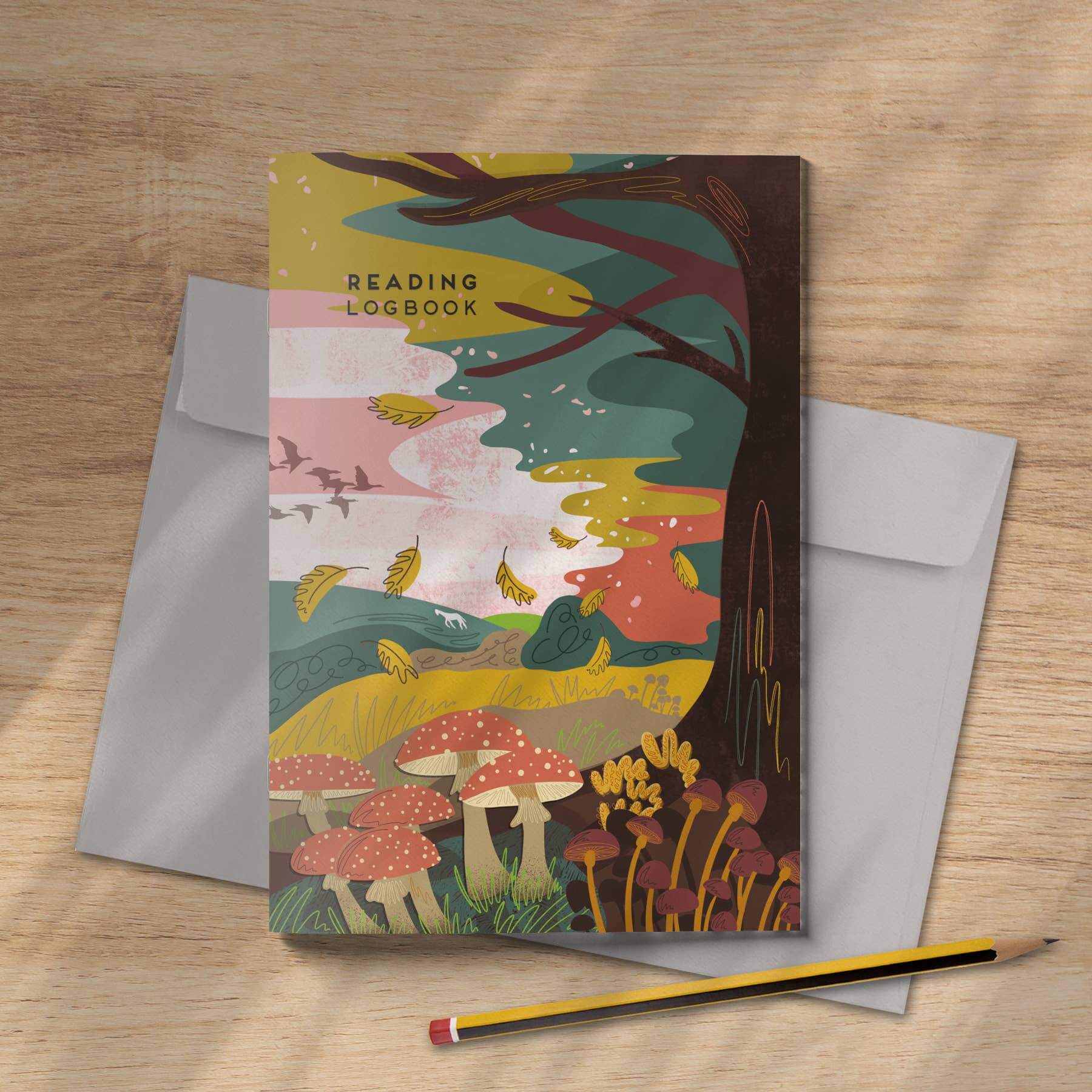 Decorative notebook with a forest design on a wooden surface with an envelope and pencil.