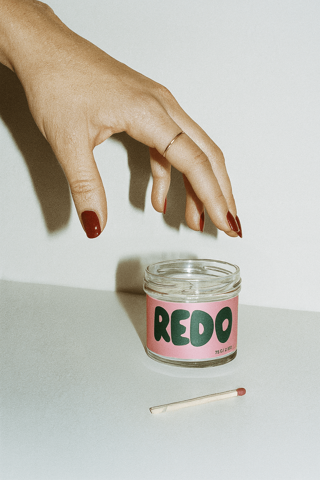 Hand holding a match above a jar labeled 'REDO' on a white background