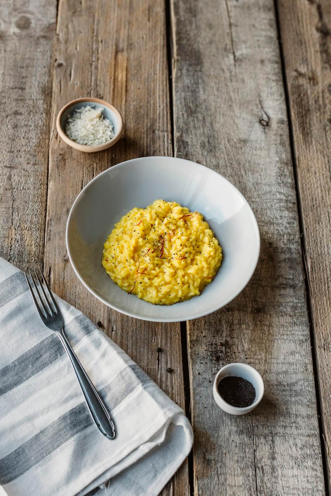 A bowl of creamy saffron risotto, with salt and pepper on a rustic wooden table, showcasing Italian cooking.