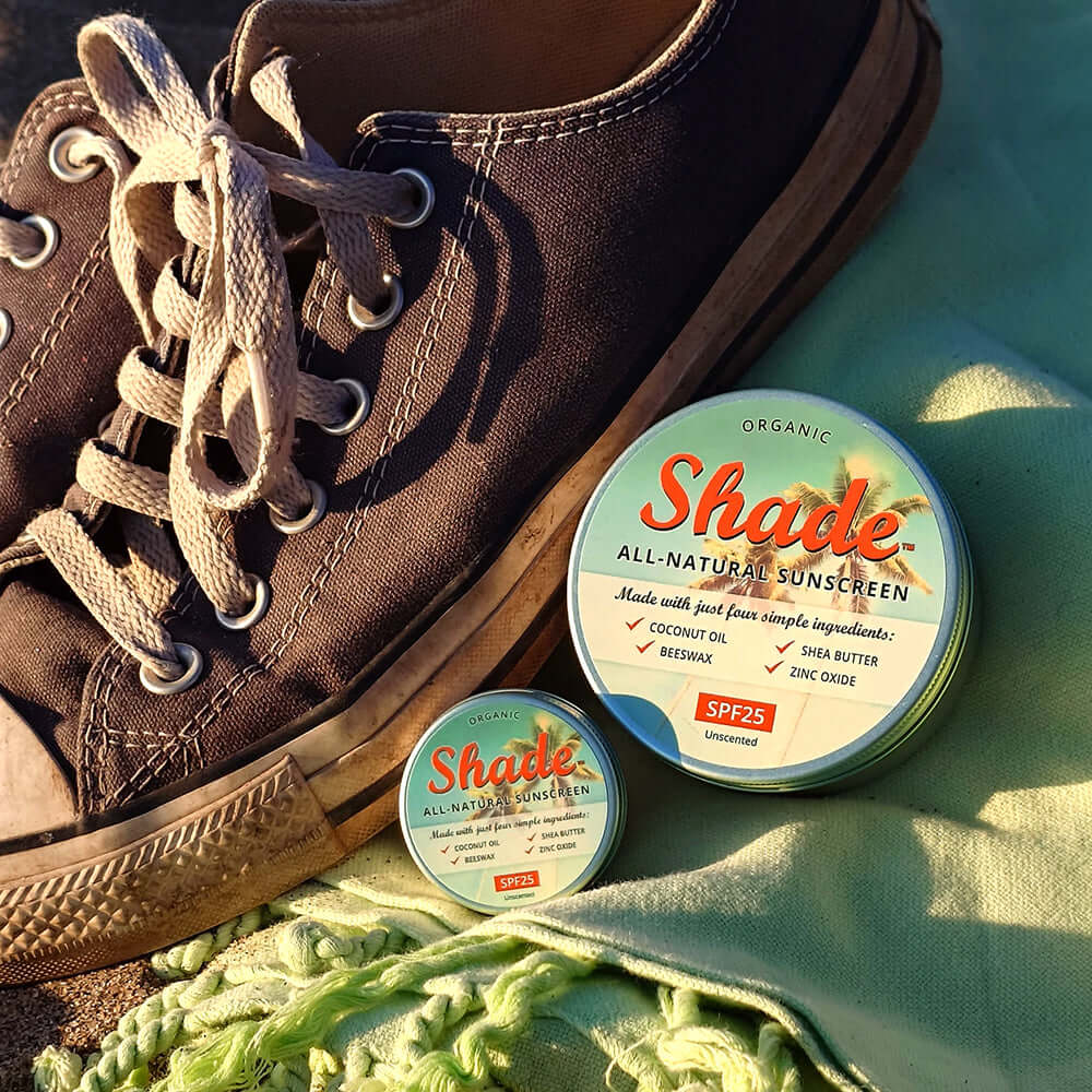 Brown sneaker with two containers of Shade sunscreen on a green surface