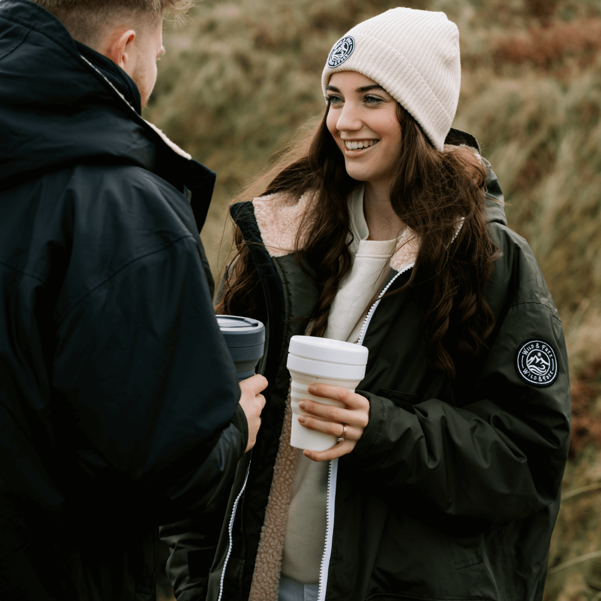 Raincoat & Changing Robe in One - The Classic Cobe Black being worn by a couple outdoors, enjoying coffee.
