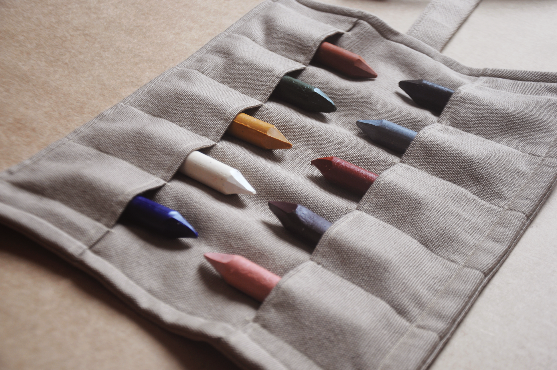 Set of colored crayons in a gray case on a beige surface