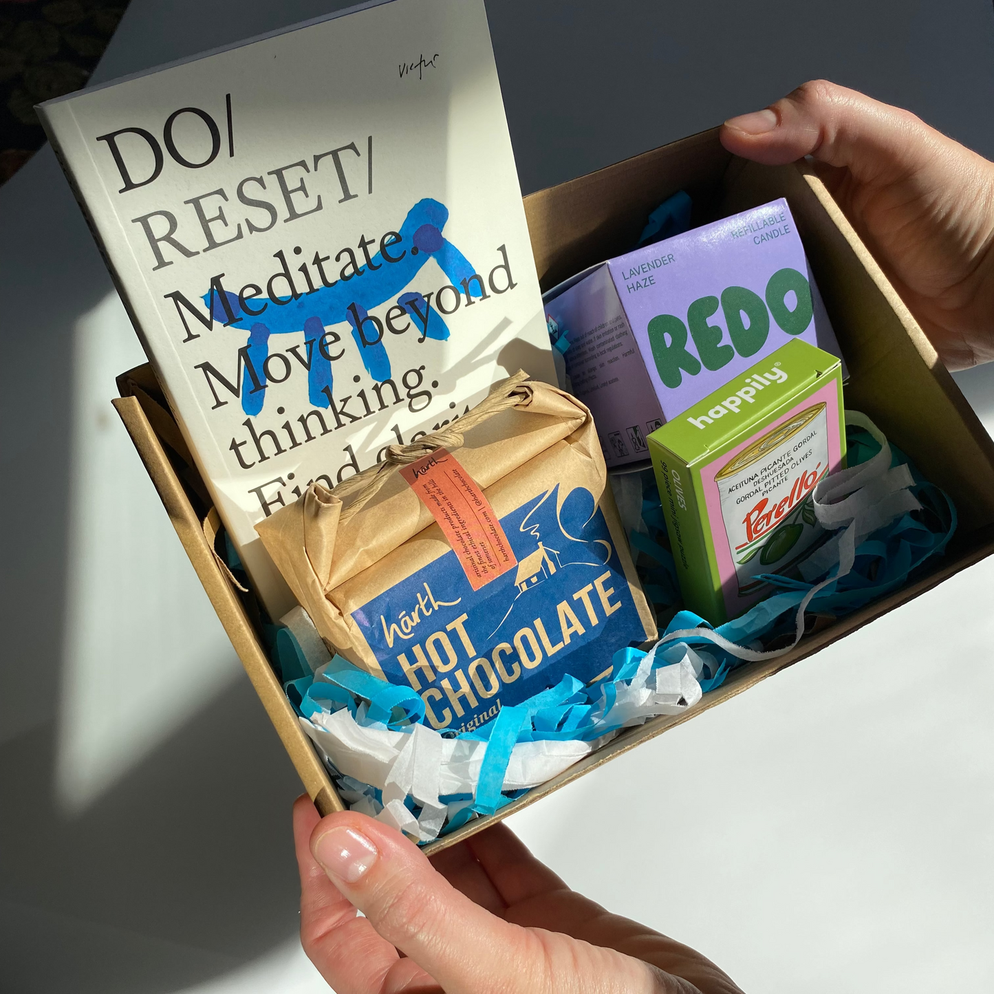 Box of items including a book, hot chocolate packets, and other products on a white surface.