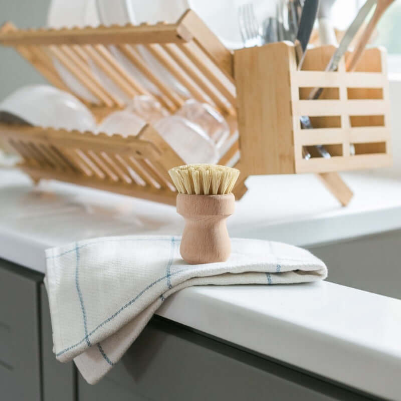 Dish brush and towel on a kitchen counter with a dish rack in the background