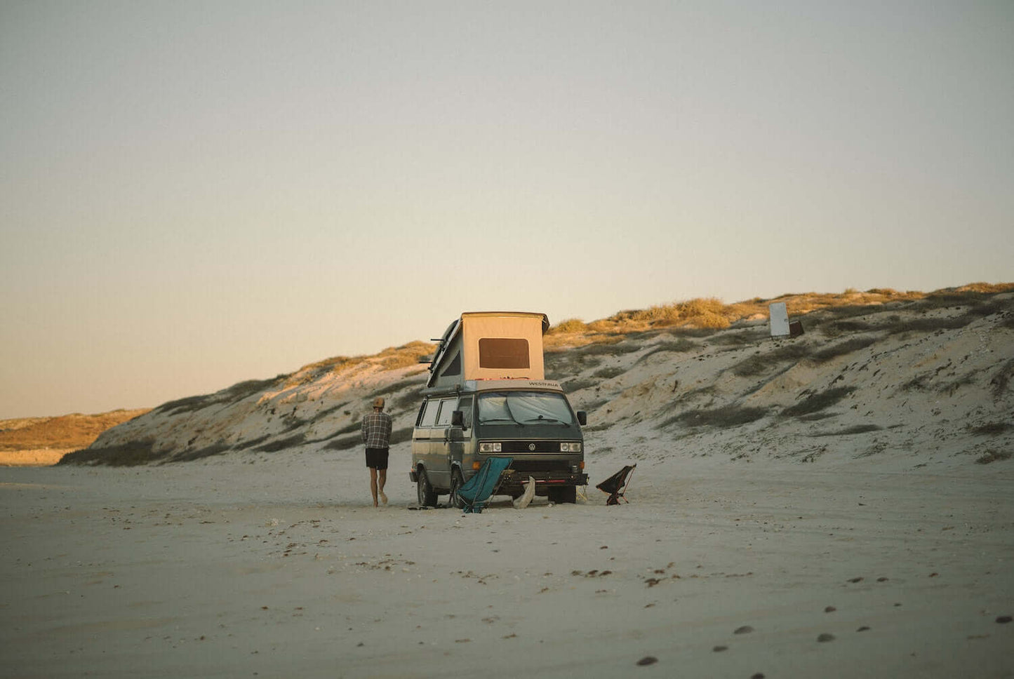 Van with a popped-top on a sandy beach with two people nearby