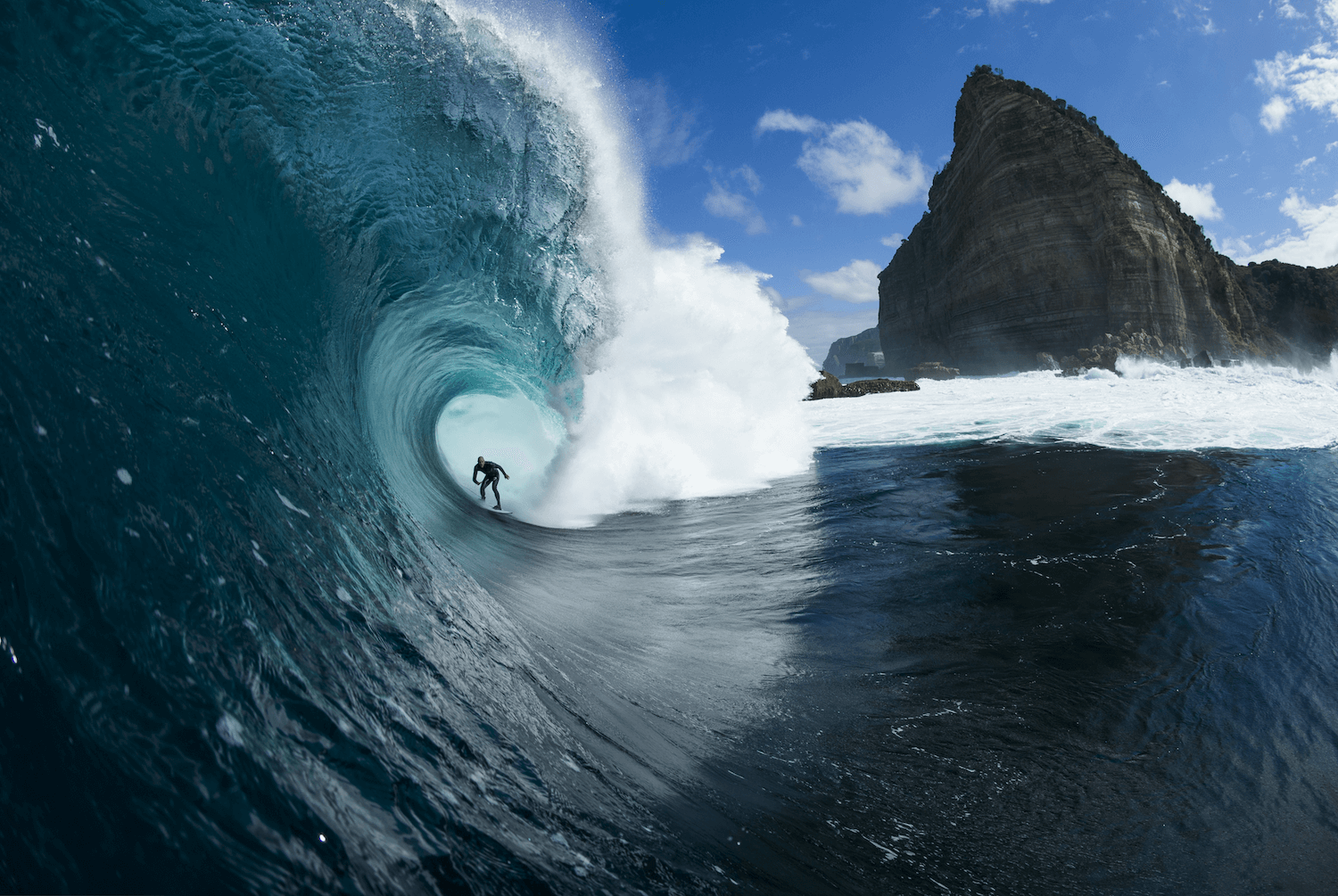 Surfer riding a large wave in the ocean with a rocky cliff in the background