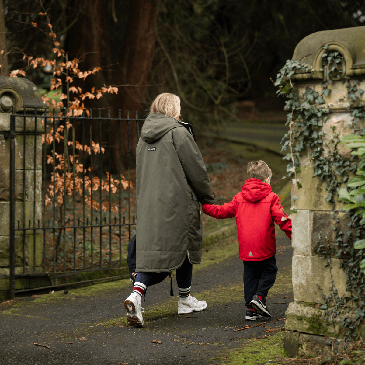 A person wearing the Raincoat & Changing Robe in One - The Classic Cobe Olive Green walks with a child.