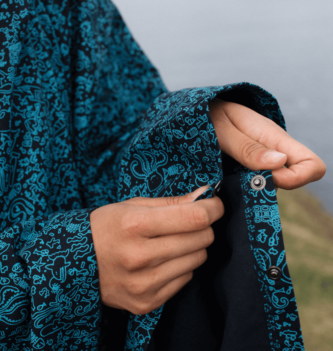 Close-up of hand adjusting a button on the Water-Repellent Rain Poncho with marine-inspired print.