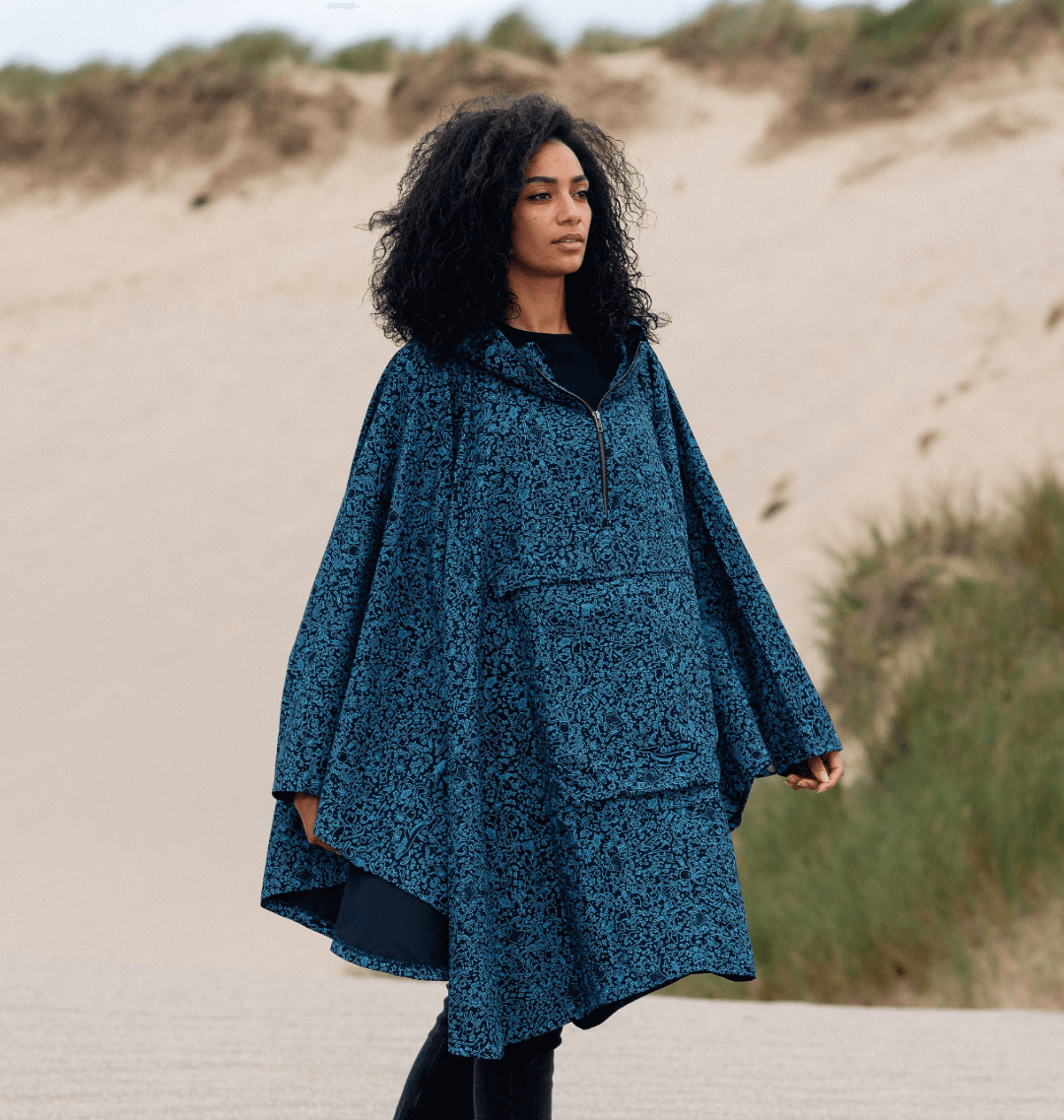 Model wearing a stylish Water-Repellent Rain Poncho with marine-inspired print on a sandy beach.