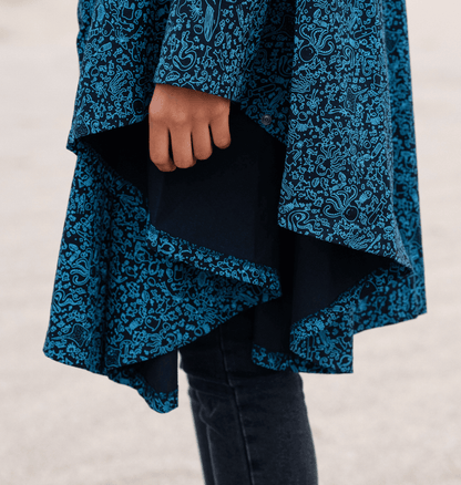 Close-up of a person's hand holding the hem of a blue marine-inspired Water-Repellent Rain Poncho.