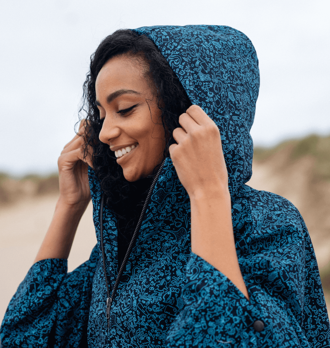 Smiling woman in a blue water-repellent rain poncho with a hood, embracing eco-friendly fashion outdoors.