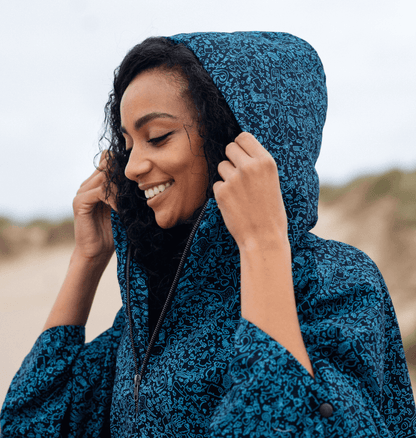 Smiling woman in a blue water-repellent rain poncho with a hood, embracing eco-friendly fashion outdoors.