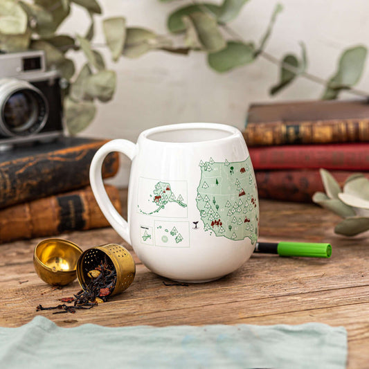 White mug with a map design on a wooden surface with books and a camera in the background