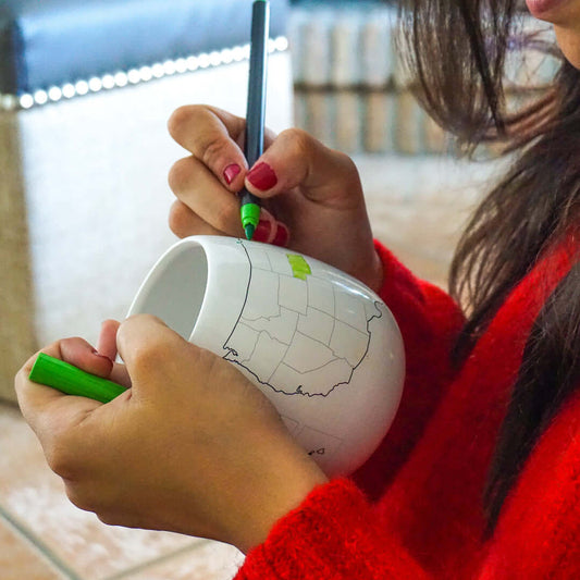 Person coloring the USA Map Colour In Travel Mug with green ceramic pen in cozy setting.