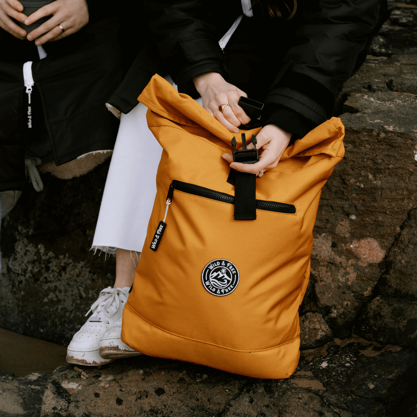 The Backpack in vibrant orange, perfect for adventures, featuring a rolled top and convenient pockets, shop at Alewk.club.