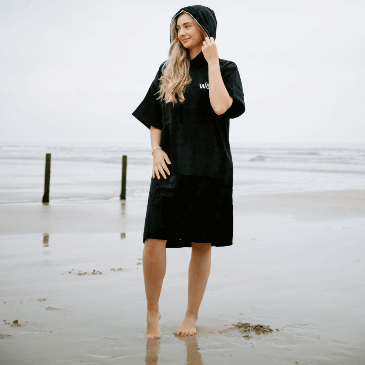 The Luxury Towel Robe on a model at the beach, showcasing its soft black organic cotton design and comfortable fit.