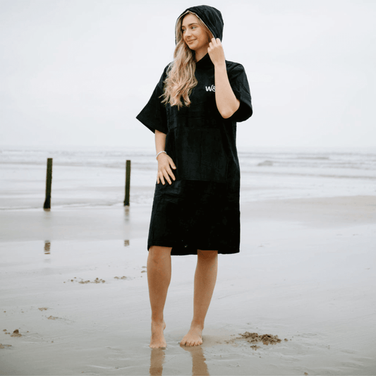 The Luxury Towel Robe on a model at the beach, showcasing its soft black organic cotton design and comfortable fit.