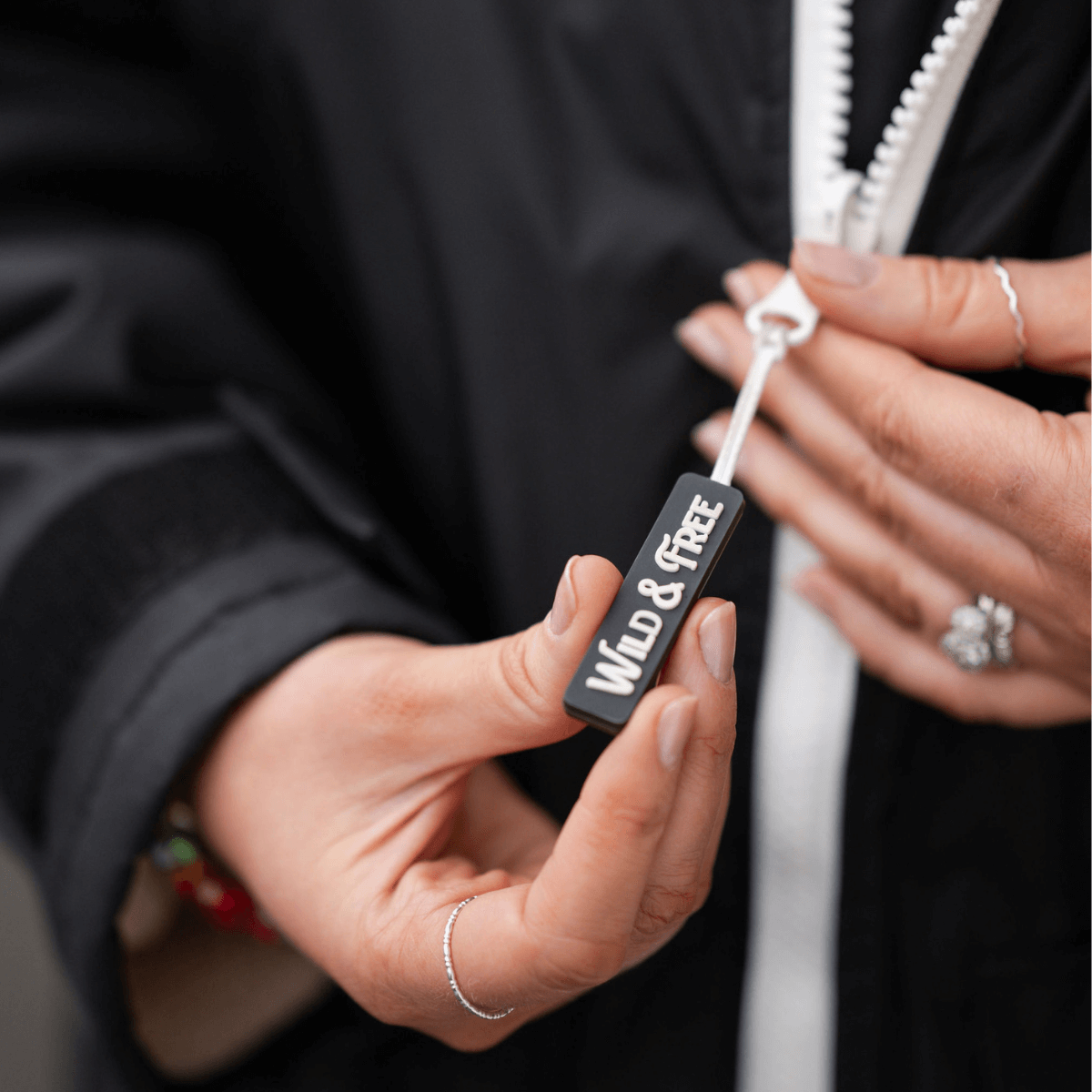 Hand holding a tag with "WILD & FREE" on a Raincoat & Changing Robe in One - The Classic Cobe Black.