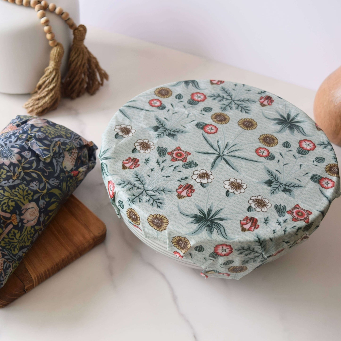 Floral-patterned container lid on a marble surface with another container and decorative elements.