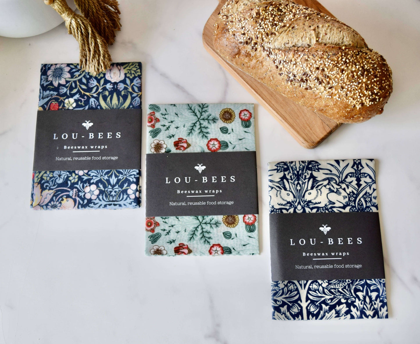 William Morris Large Beeswax wrap singles displayed with fresh bread on a marble countertop.