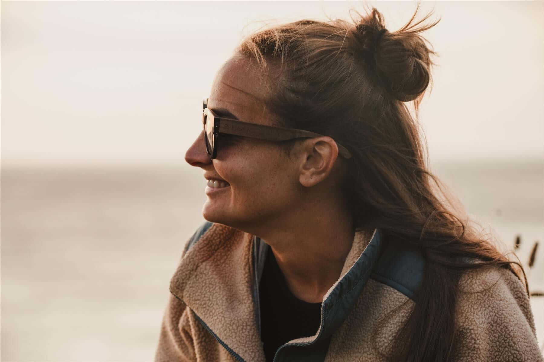 Luma Sunglasses - Polzeath - Smoke worn by a woman enjoying the natural beauty of the seaside, showcasing eco-friendly style.