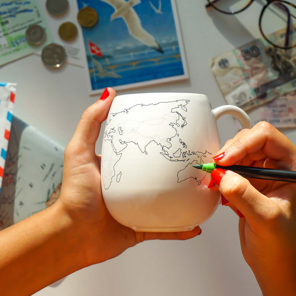 Person drawing a world map on a mug with a pen.