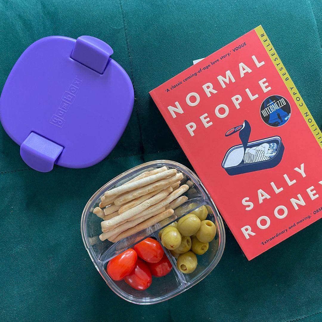 Yumbox Leakproof Snack Bowl - 3 Compartment with snacks and book on a green background.